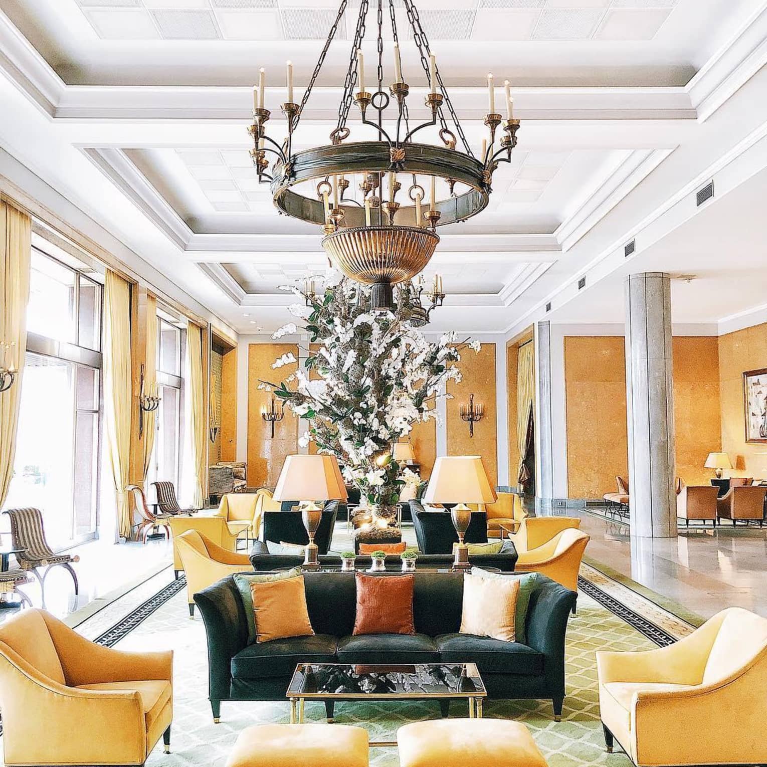 Chandelier over hotel lobby seating area with yellow chairs, footrests and curtains