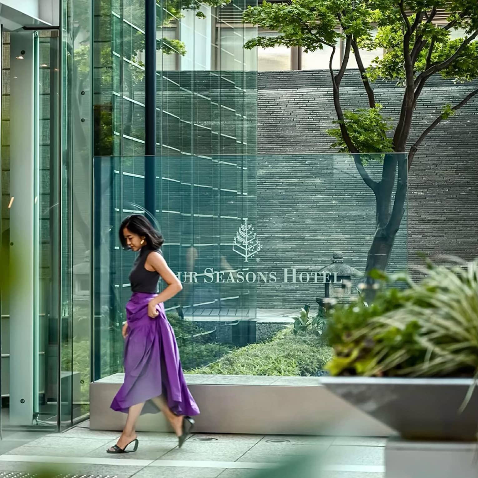 Person in a purple skirt walking past the glass entrance of Four Seasons 