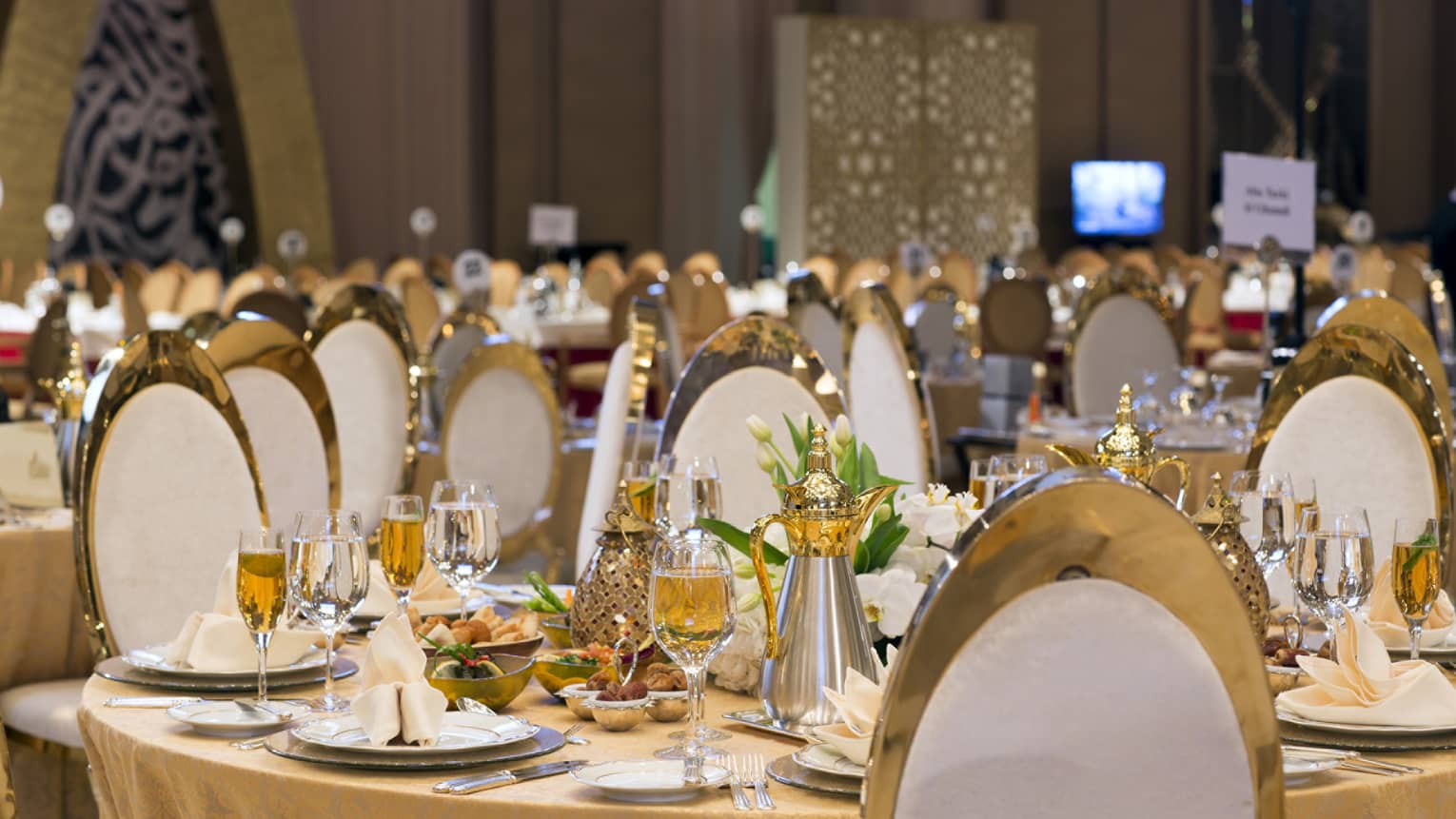 Round table set for dinner with wine glasses, flowers, napkins and white and gold chairs