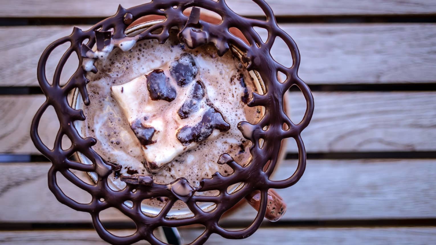 A cup of hot chocolate with a chocolate pattern extending out of the cup.