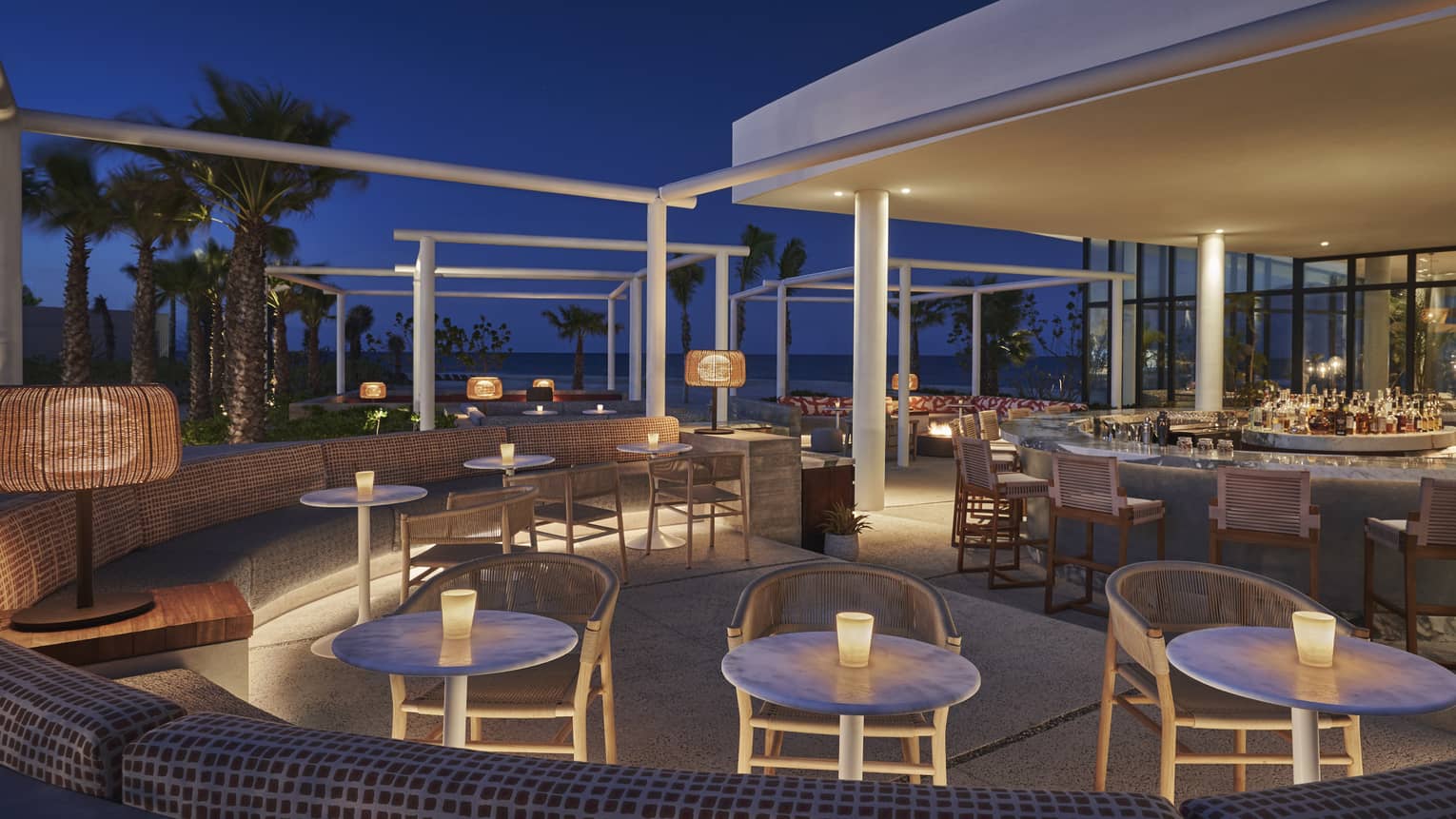 More than 10 round tables with candles on top are set up on the outdoor terrace at Milos Bar at night 