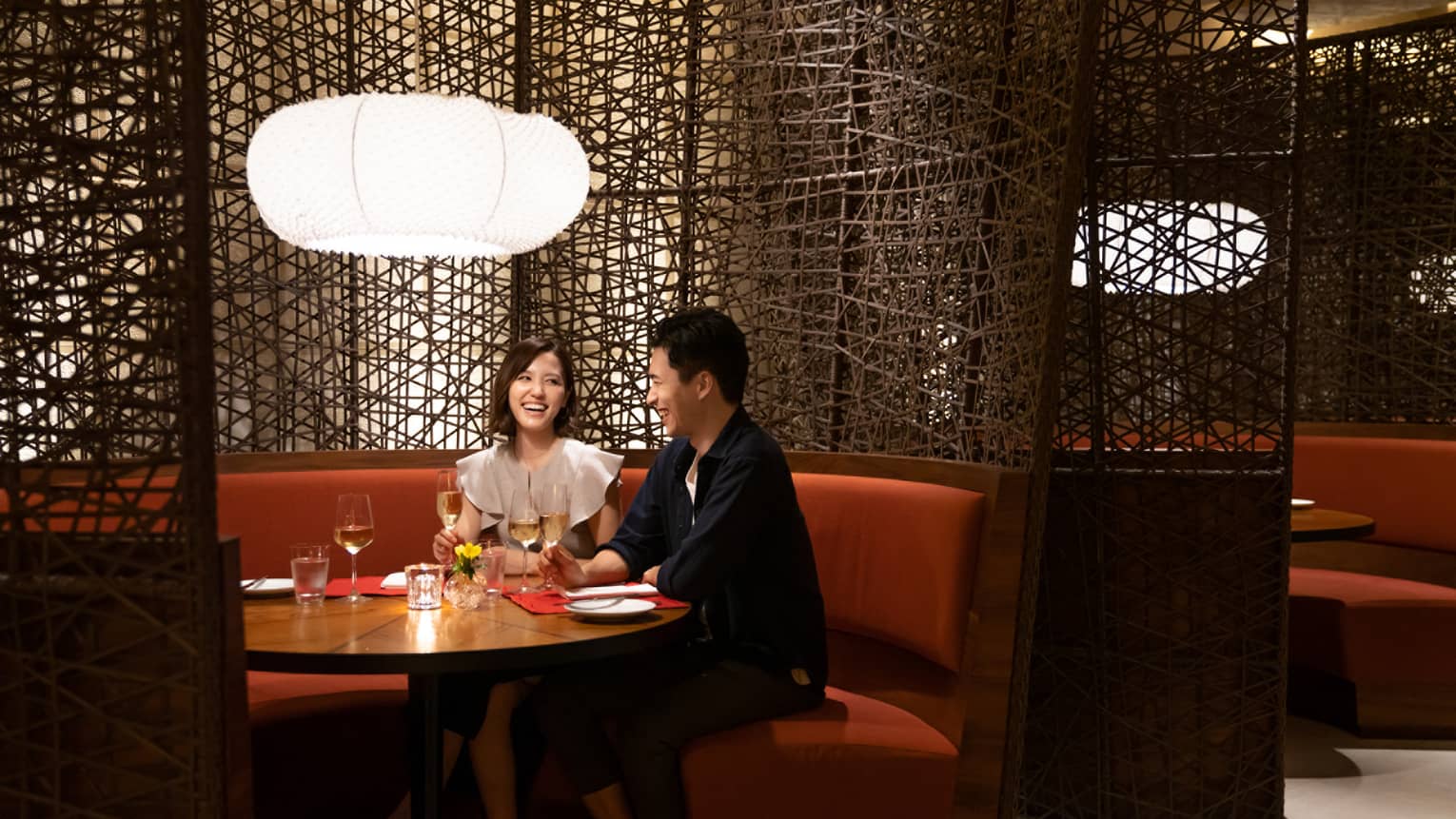Woman and man smile at each other at rounded booth table in restaurant at Four Seasons Hotel Kyoto