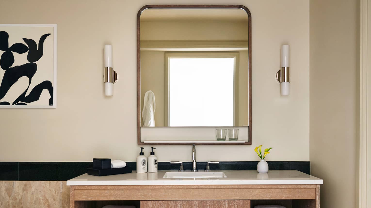 Bathroom with wood and marble vanity, abstract black and white artwork on the wall, mirror and two sconces