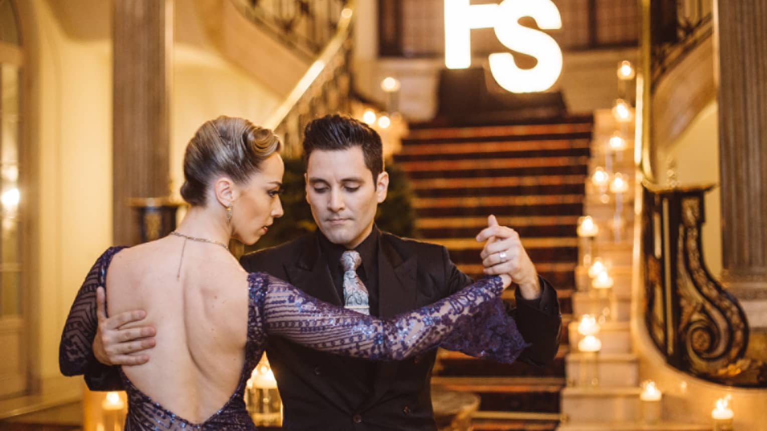 A man and woman tango dancing at the bottom of a wide red carpeting stairway