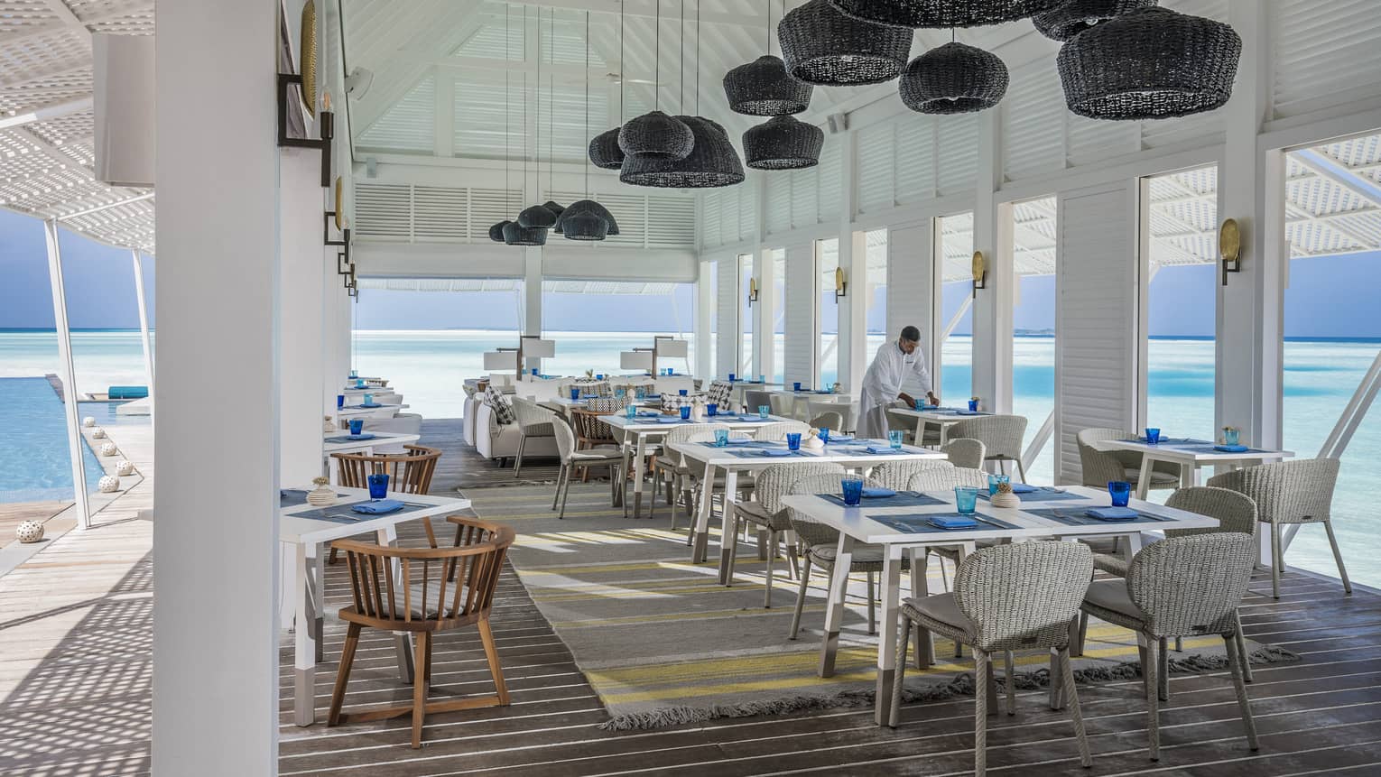 Wicker lanterns hang above clean place-settings adjacent to the ocean at the Blu Beach Club