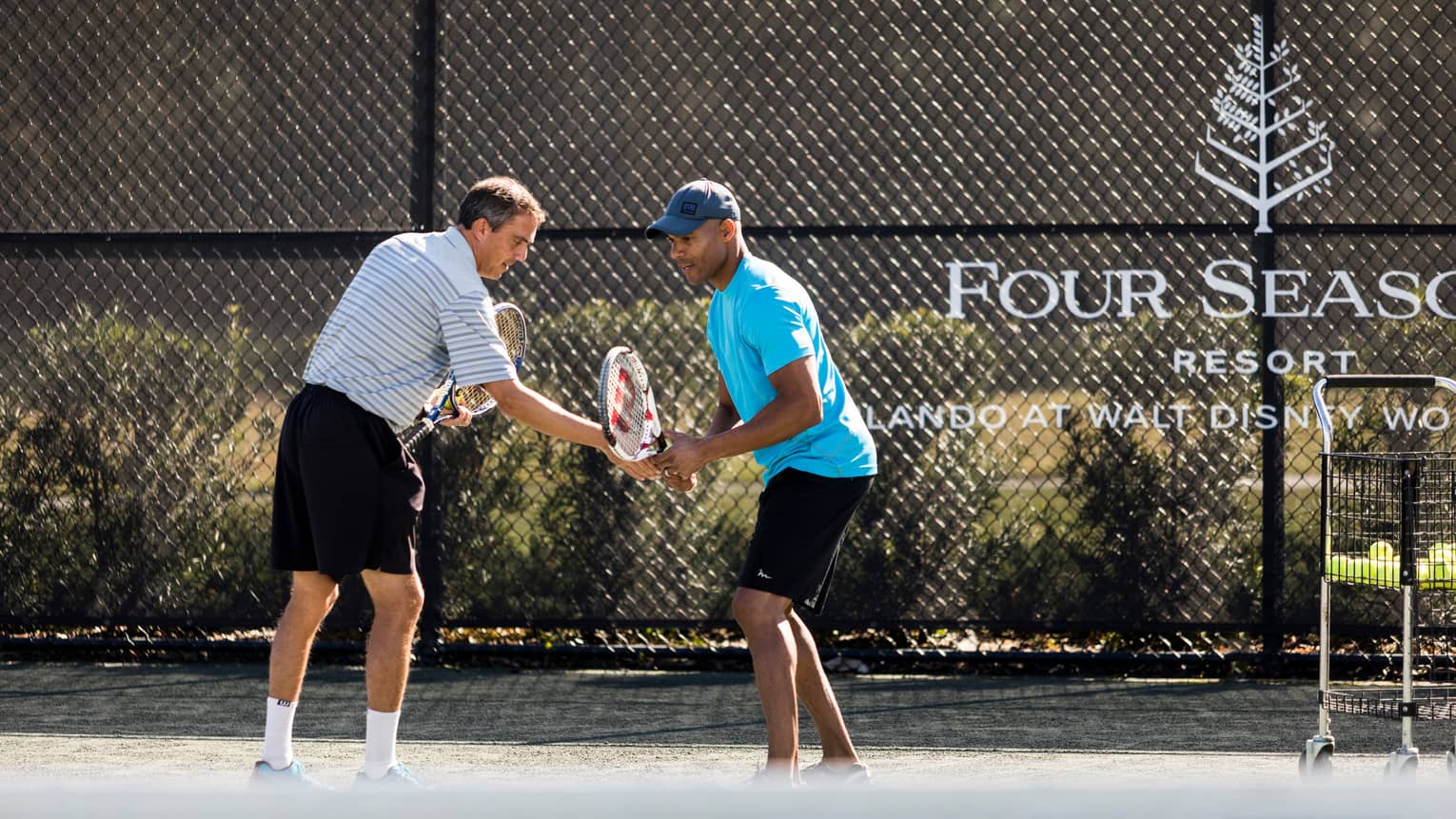 Tennis pro helps man adjust his racket on tennis court by Four Seasons Resort logo on fence