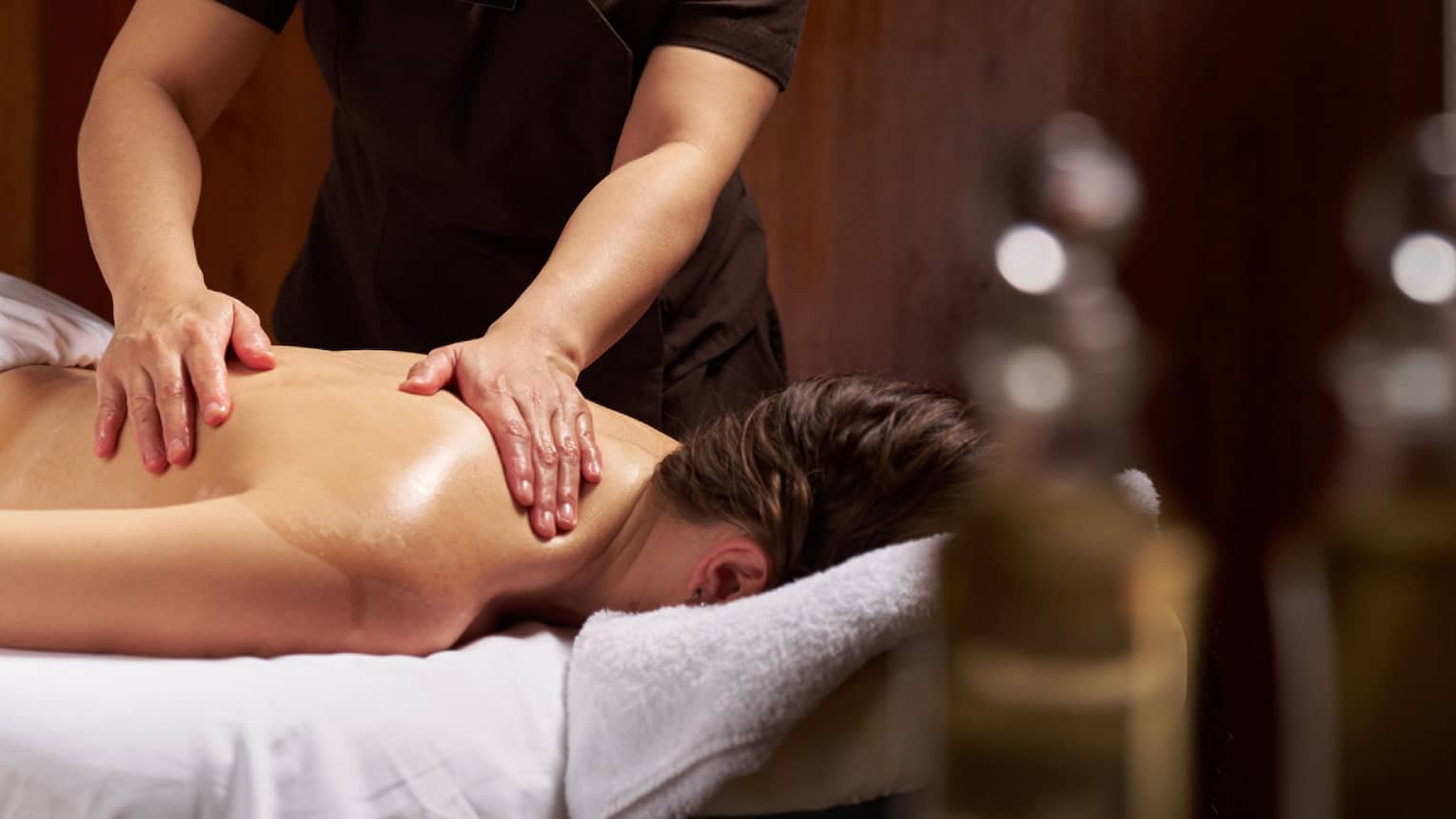 Masseuse performs treatment on female guest lying face down on massage table