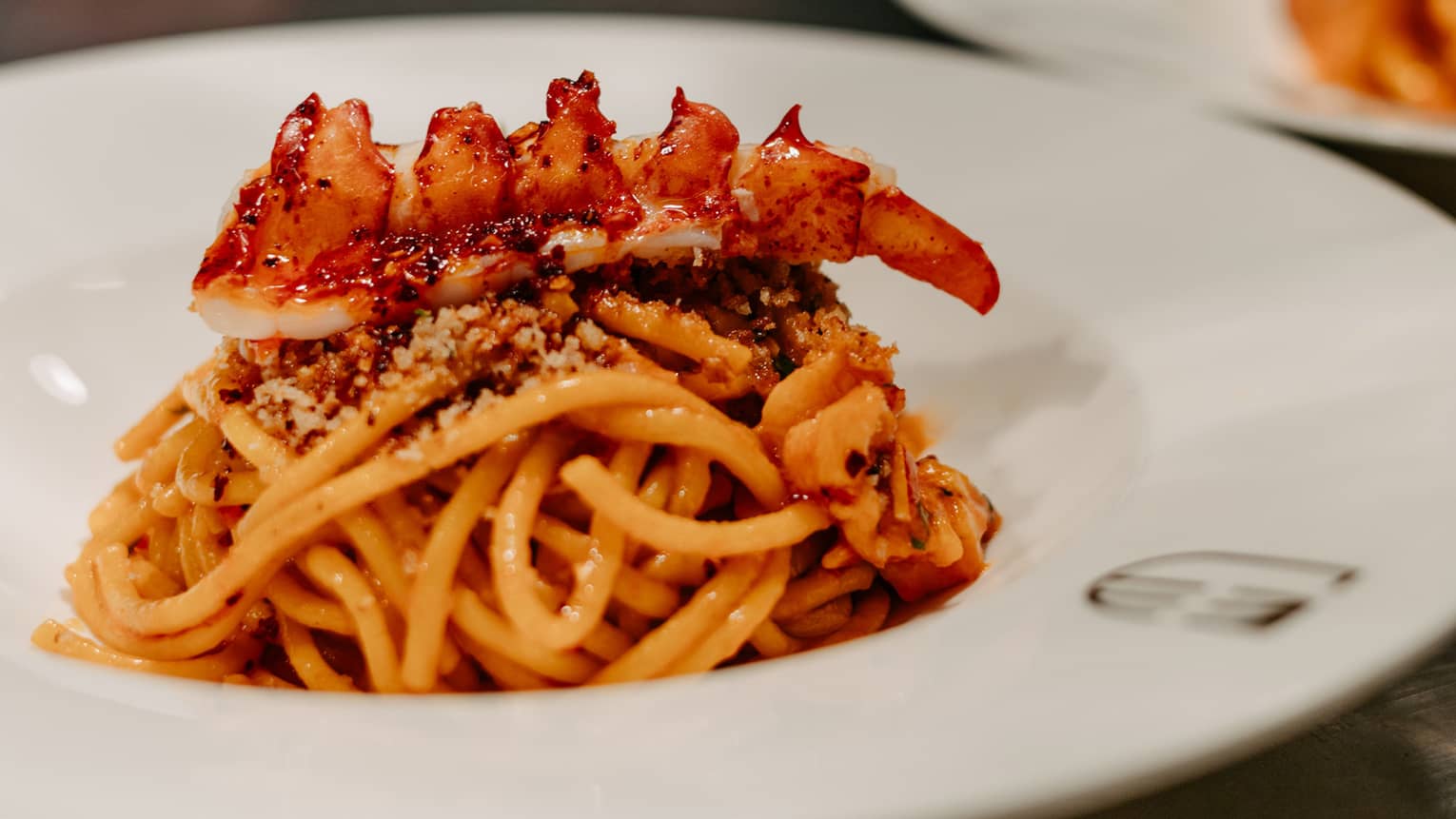 Mound of pasta topped with lobster in white bowl