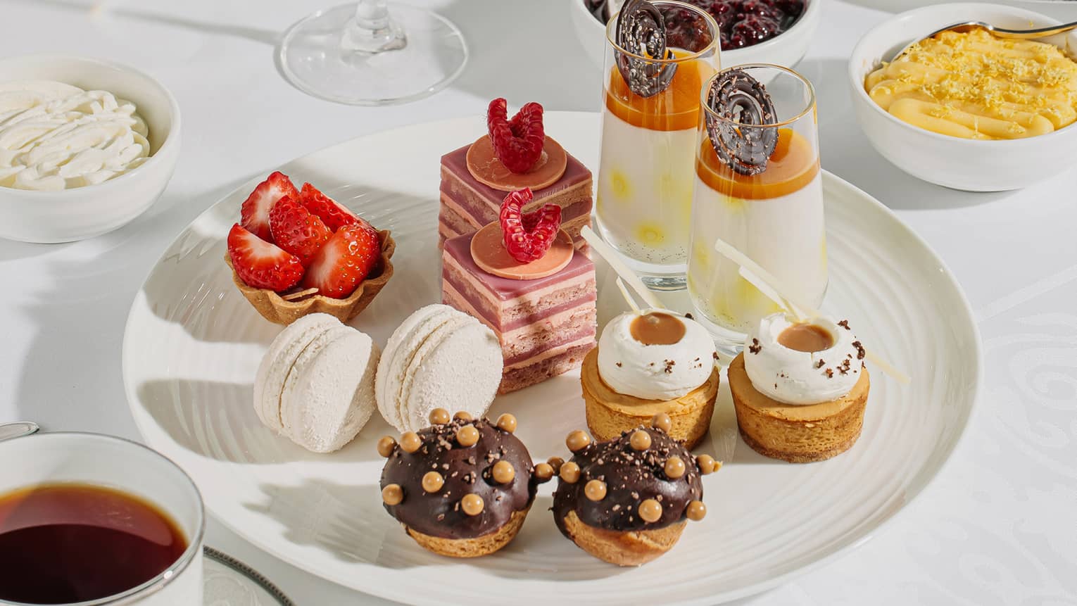A plate holding artfully decorated pastries rests on a table amidst glasses of sparkling wine and sides of jam and custard.