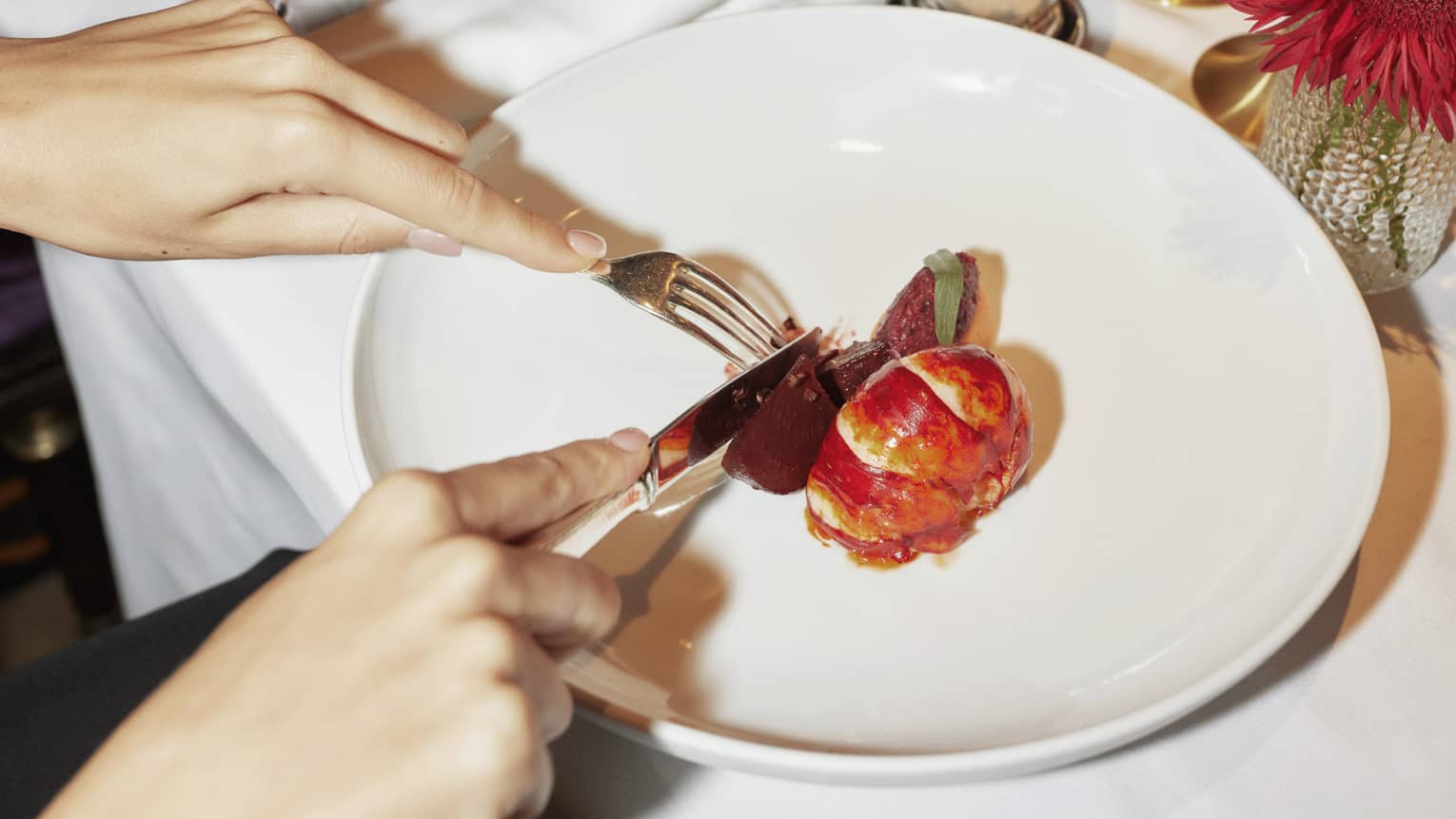 Two people sit at white-cloth table, cutting into contemporary dish on large white plate