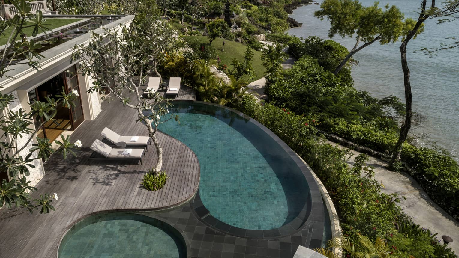 Looking down at Imperial Villa swimming pool and whirlpool on deck with white lounge chairs, garden path and ocean below