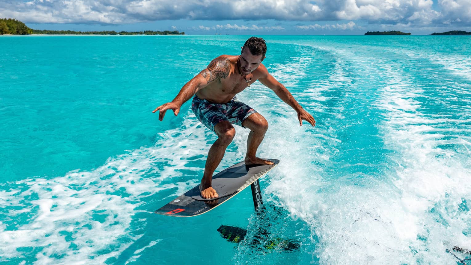 A guest balancing on an electric surfboard, arms outstretched as they soar above the wake in the clear turquoise waters.
