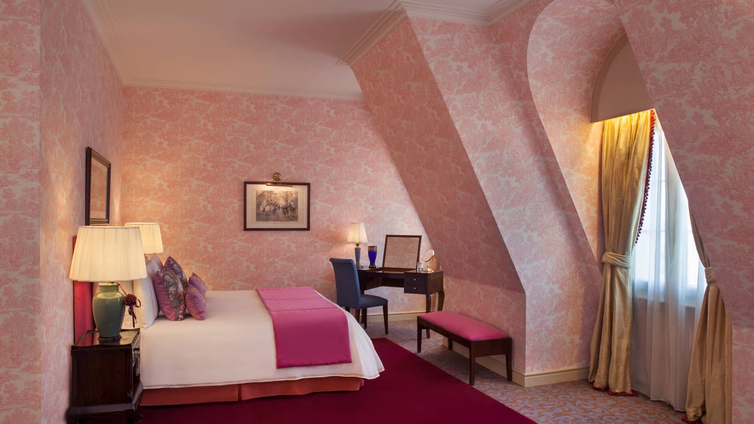 La Mansión Diplomatic Premier Suite with pink-patterned wallpaper on sloped walls, bed, bench and desk
