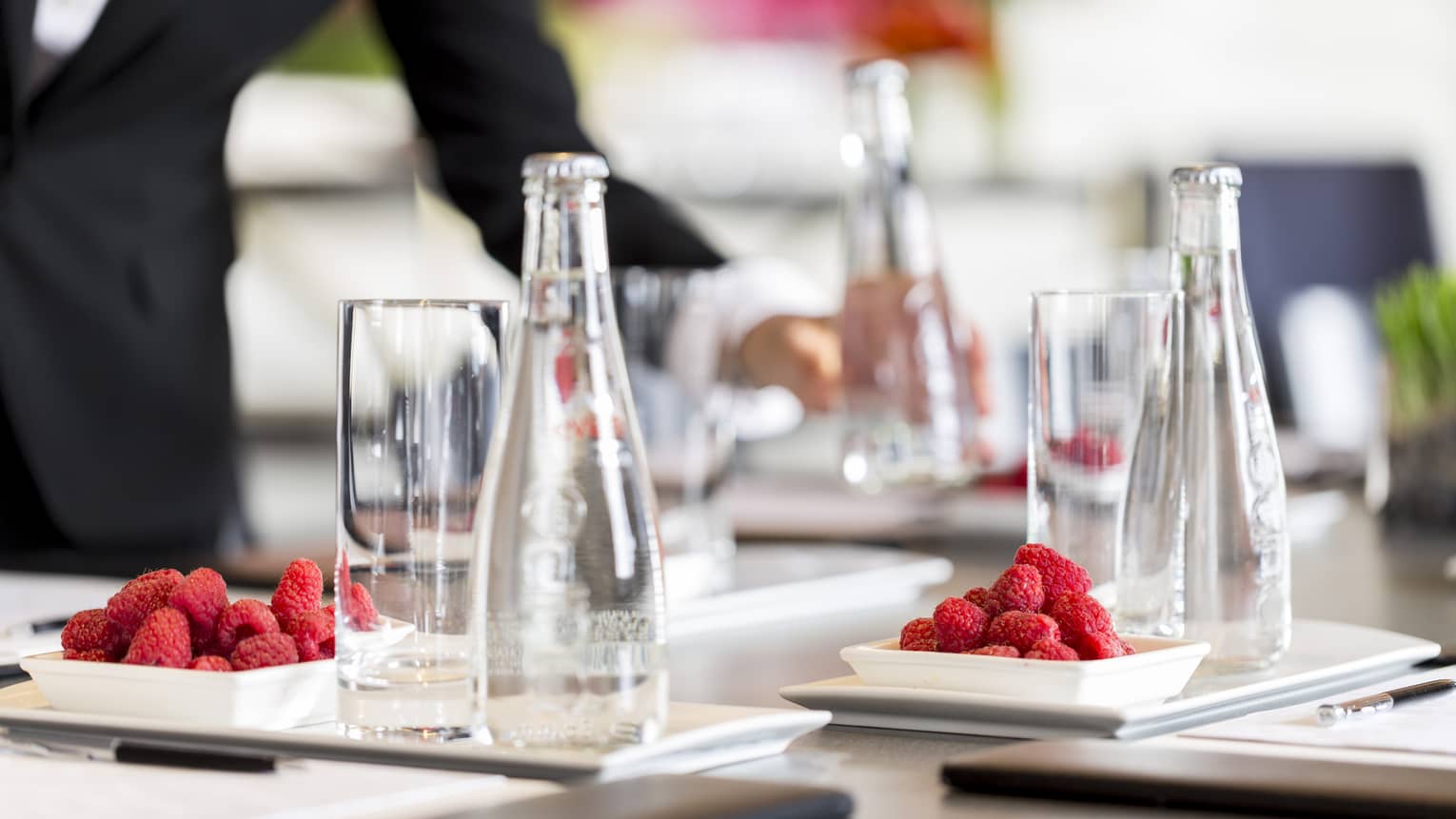 Glass bottles of water and plates of raspberries are set in preparation for a meeting