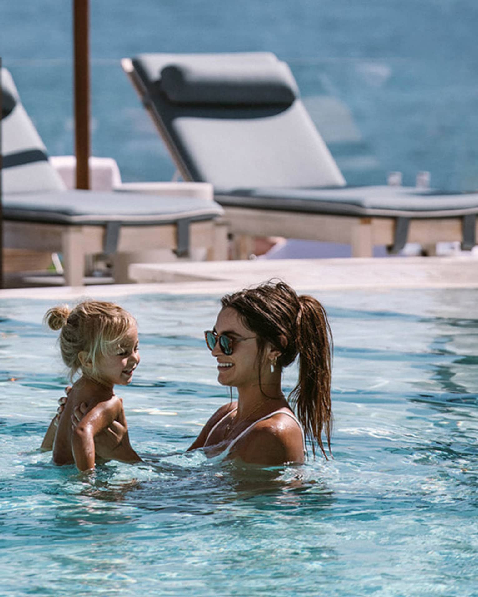 Adult and holds a young shild in a pool, both smiling