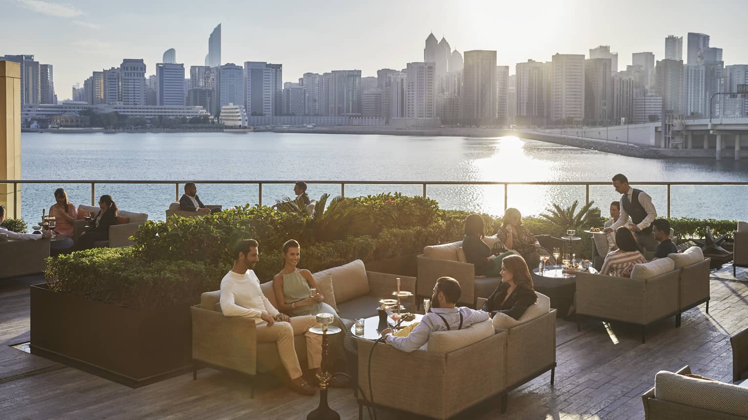 People mingling on sofas of outdoor terrace, overlooking sea and Abu Dhabi city