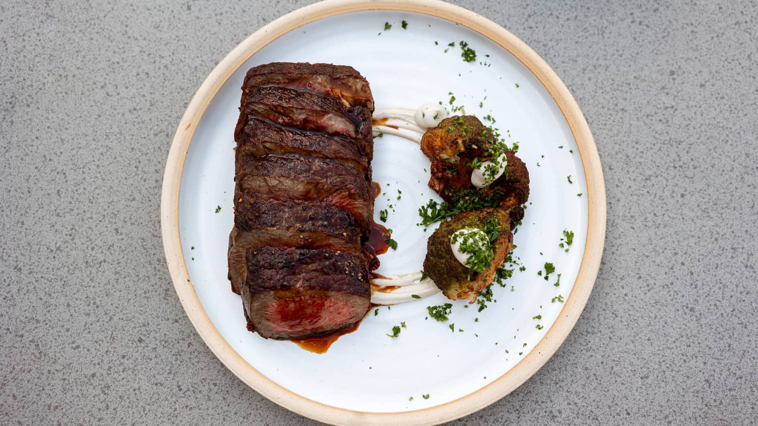 A round white plate holds a cooked piece of meat and a side item.