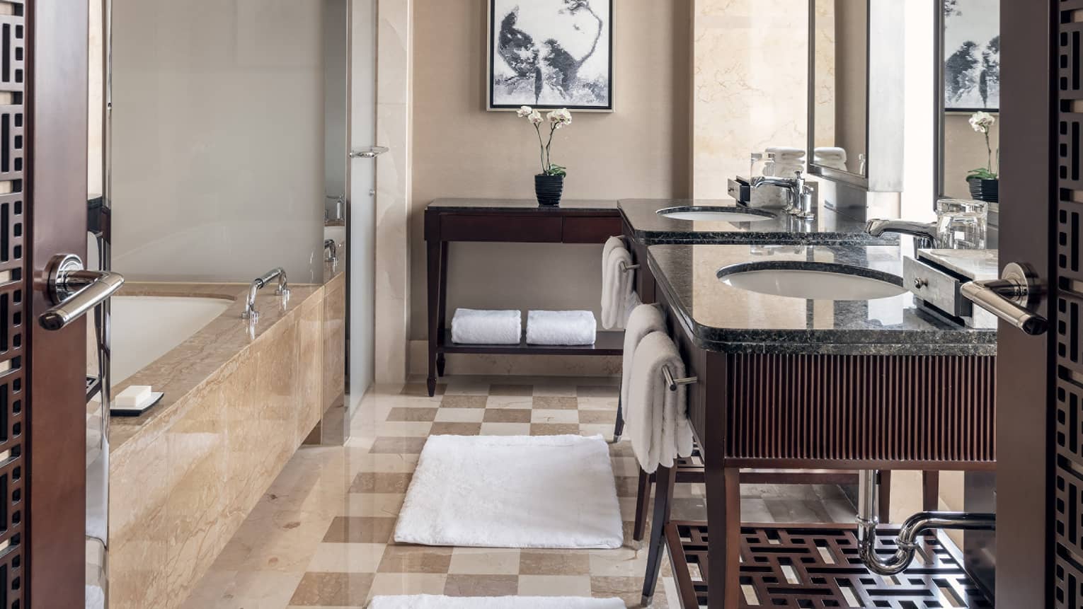 Bathroom with tan and cream square tiled floor, dark wooden vanity, tub and glass shower