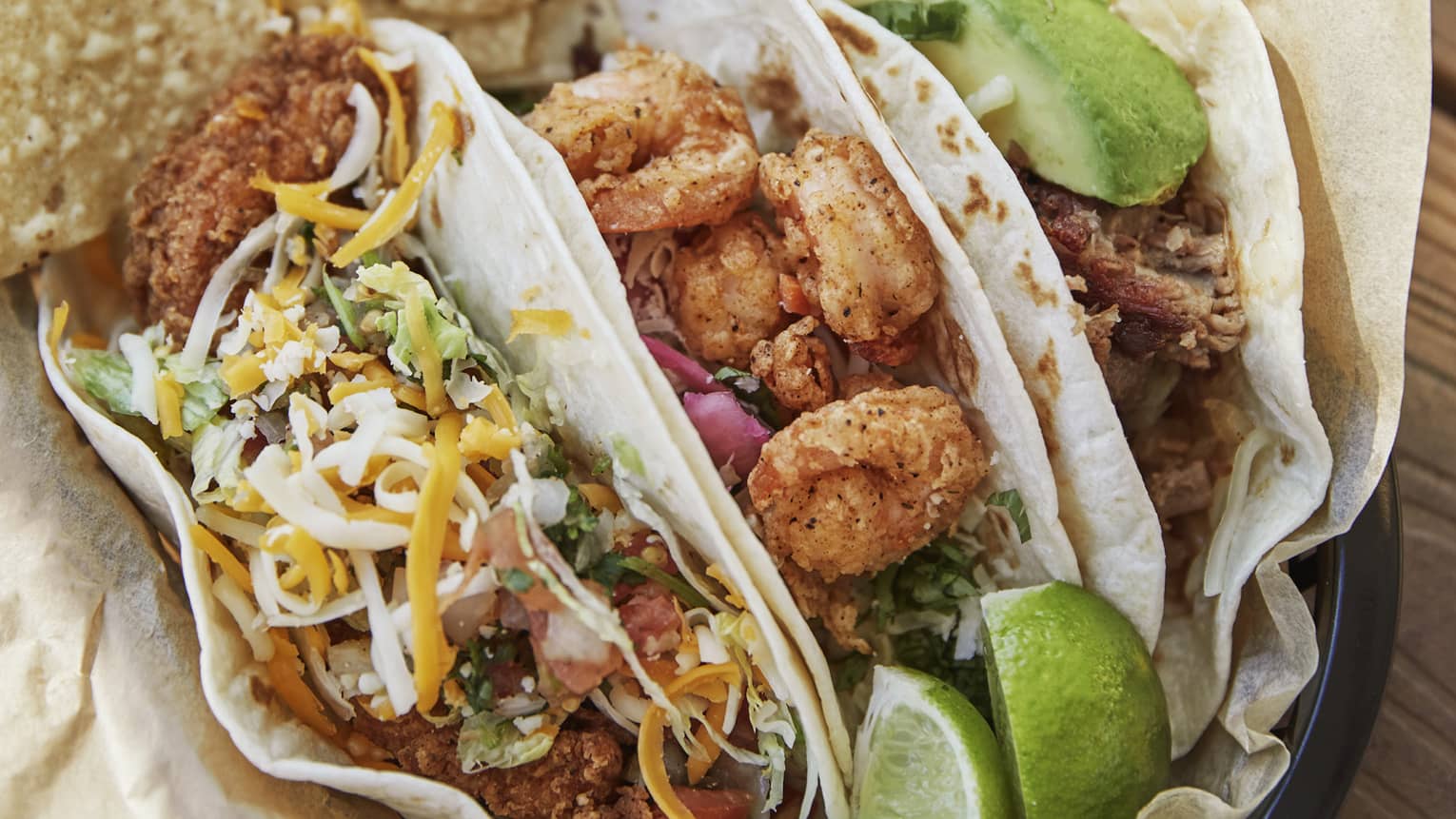 Three shrimp tacos in a basket served with tortilla chips and lime wedges