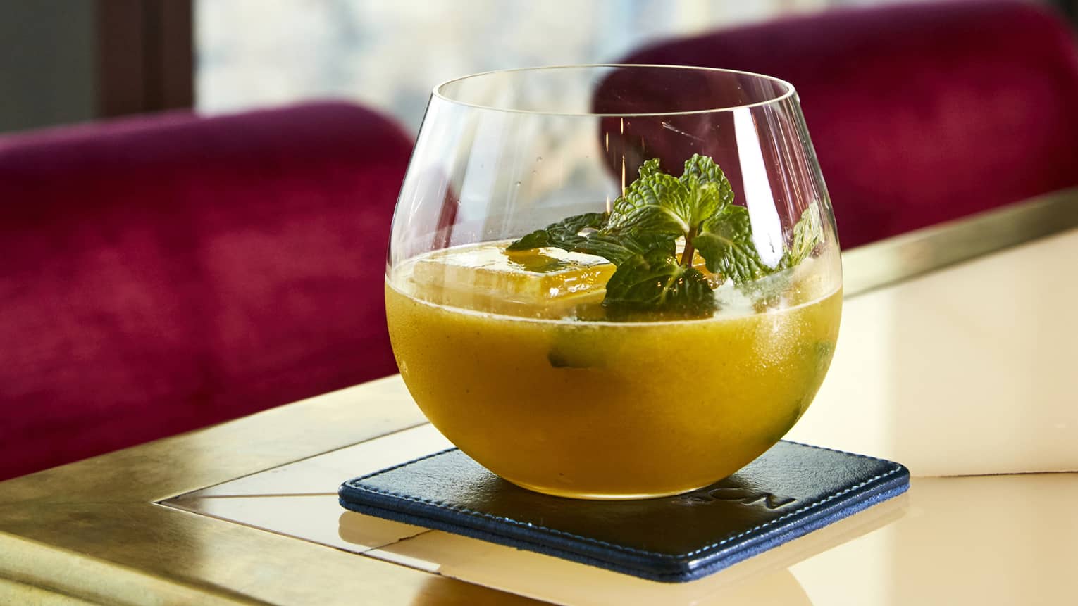An orange beverage in a rounded glass topped with several sprigs of mint.