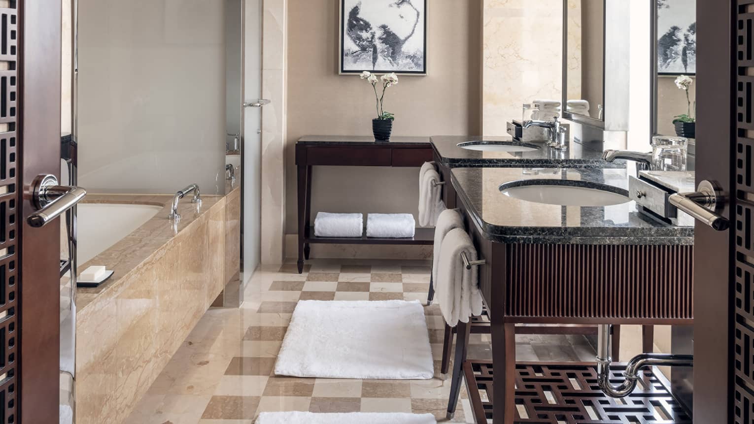 Bathroom with tan and cream square tiled floor, dark wooden vanity, tub and glass shower