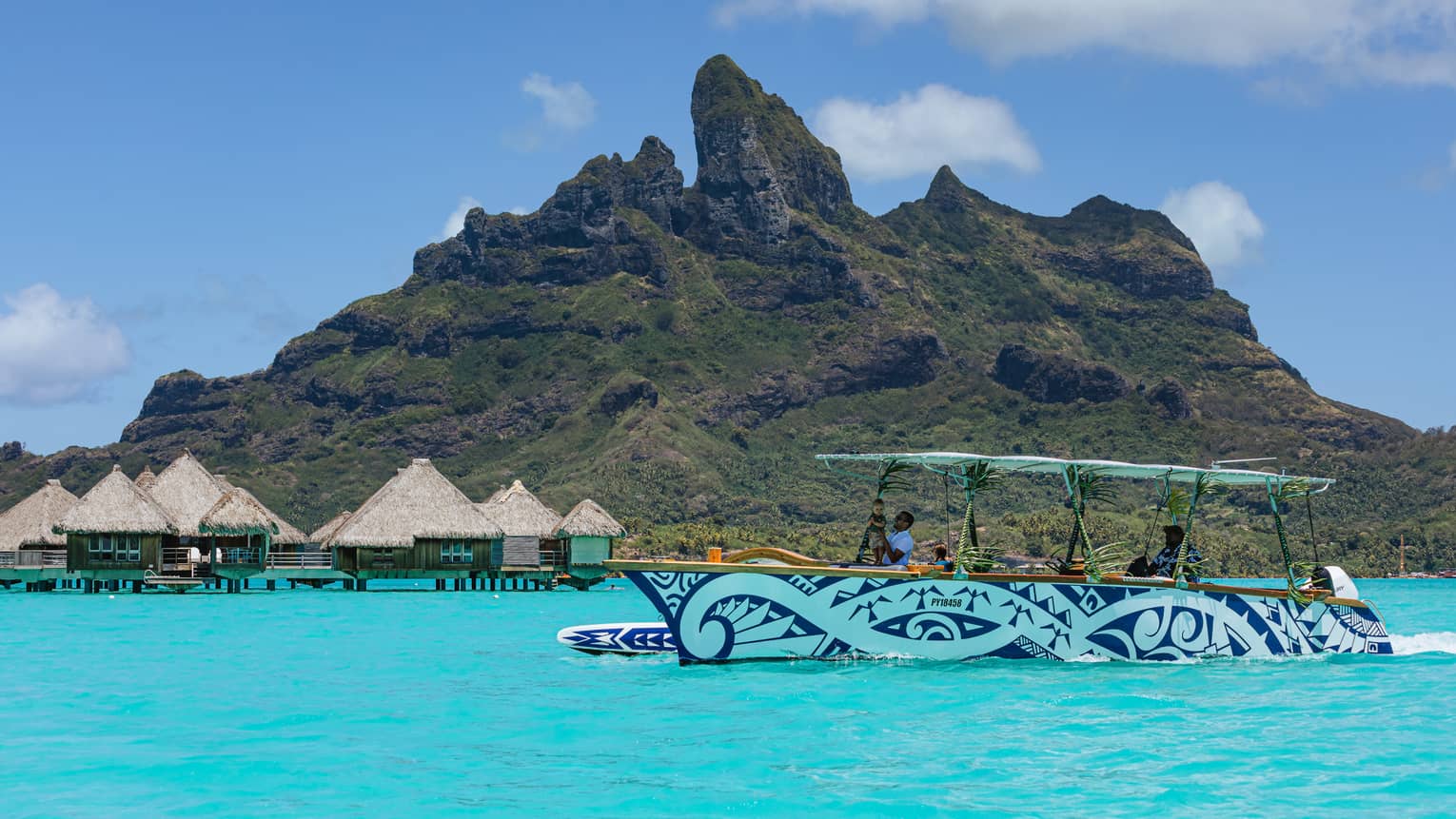 Blue and white patterned boat cruises along turquoise waters with lush green mountains in background