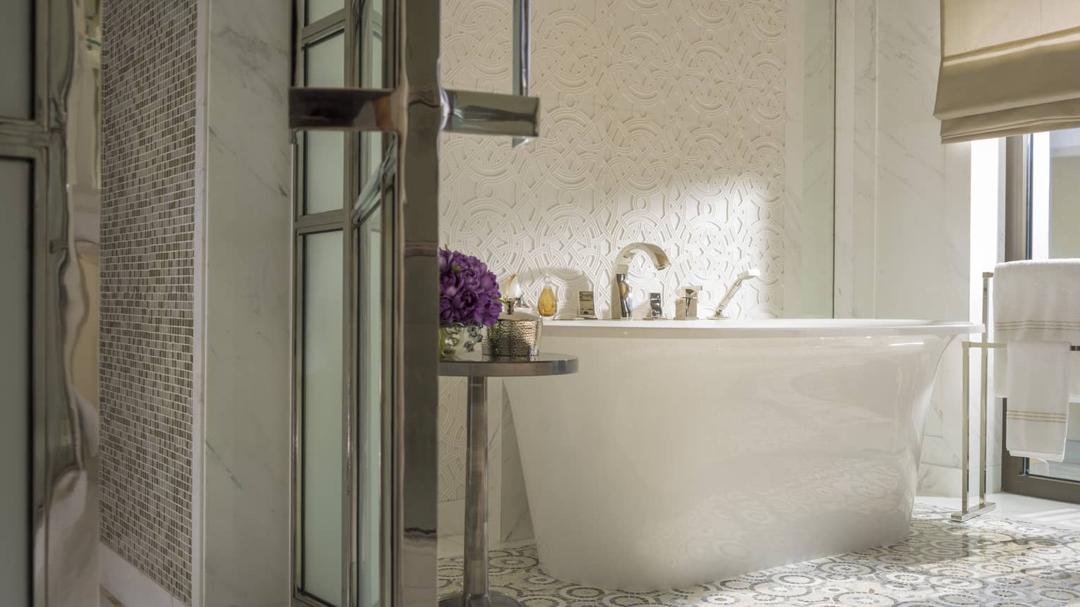 Bathroom with mosaic tile floor and free-standing tub next to a textured wall and window