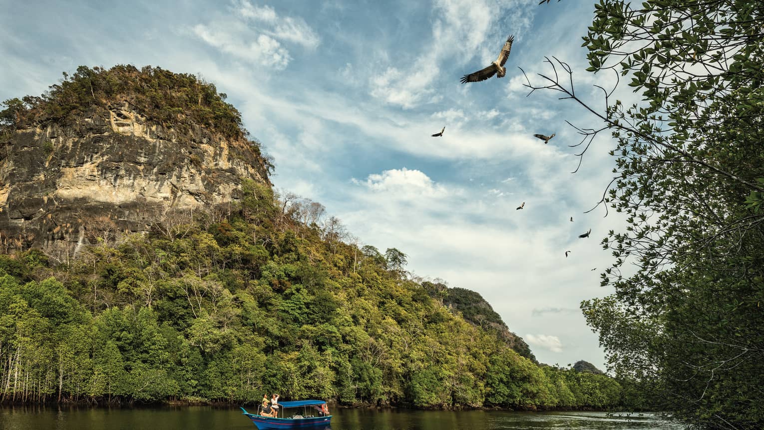 People on small blue boat on river under small rocky mountain