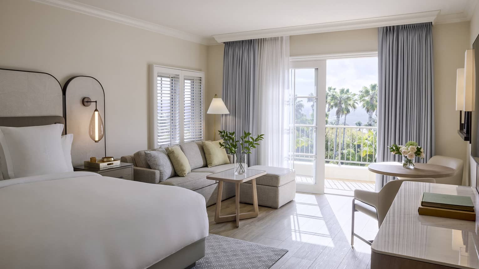 Elegant residential room with king bed, sitting area with sofa, table with two chairs, and balcony