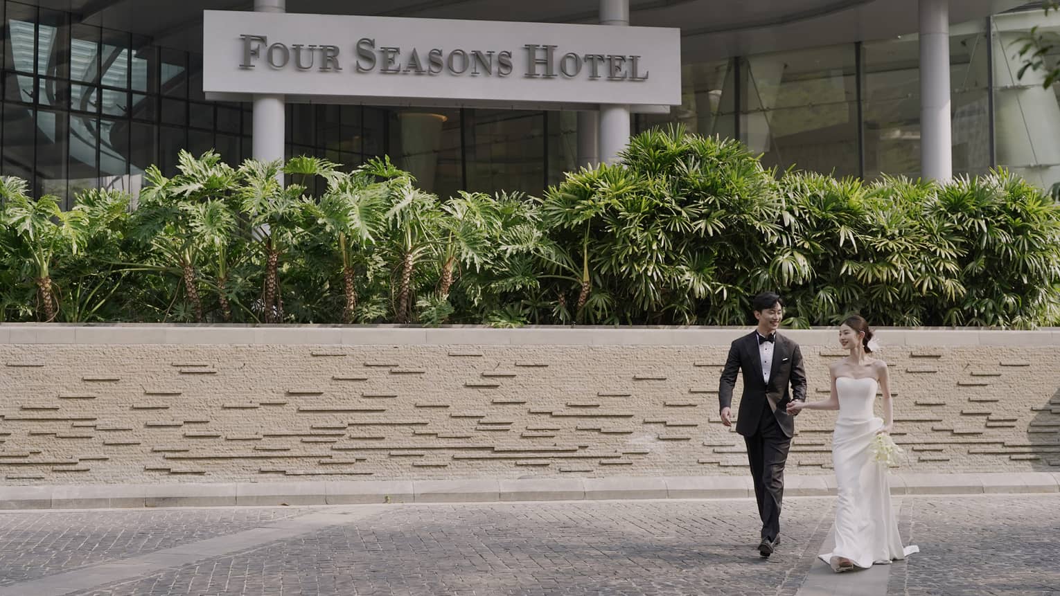 Bride and groom walk in front of hotel showing Four Seasons Hotel sign