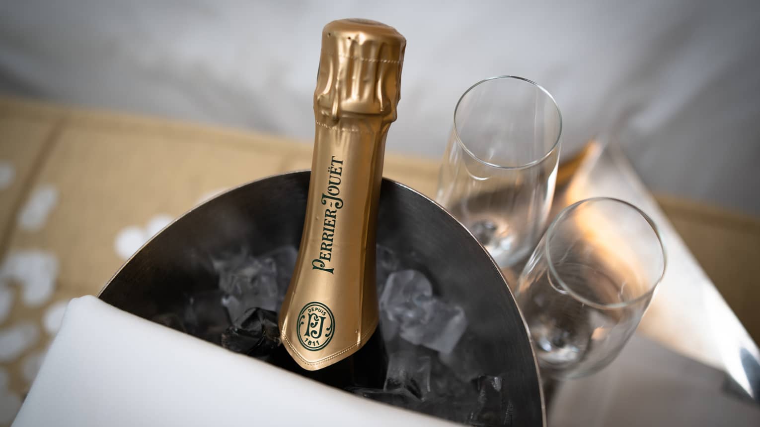 A bottle of Champagne in a bucket of ice with two glasses next to it.