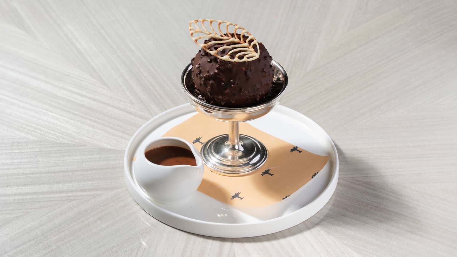 Vanilla bean ice cream covered in chocolate and served in a stemmed metal glass with a side of chocolate sauce