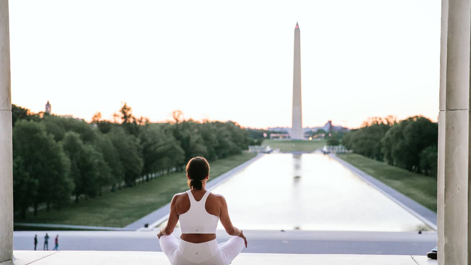 A woman in workout clothes is sitting and looking at the Washington Monument.