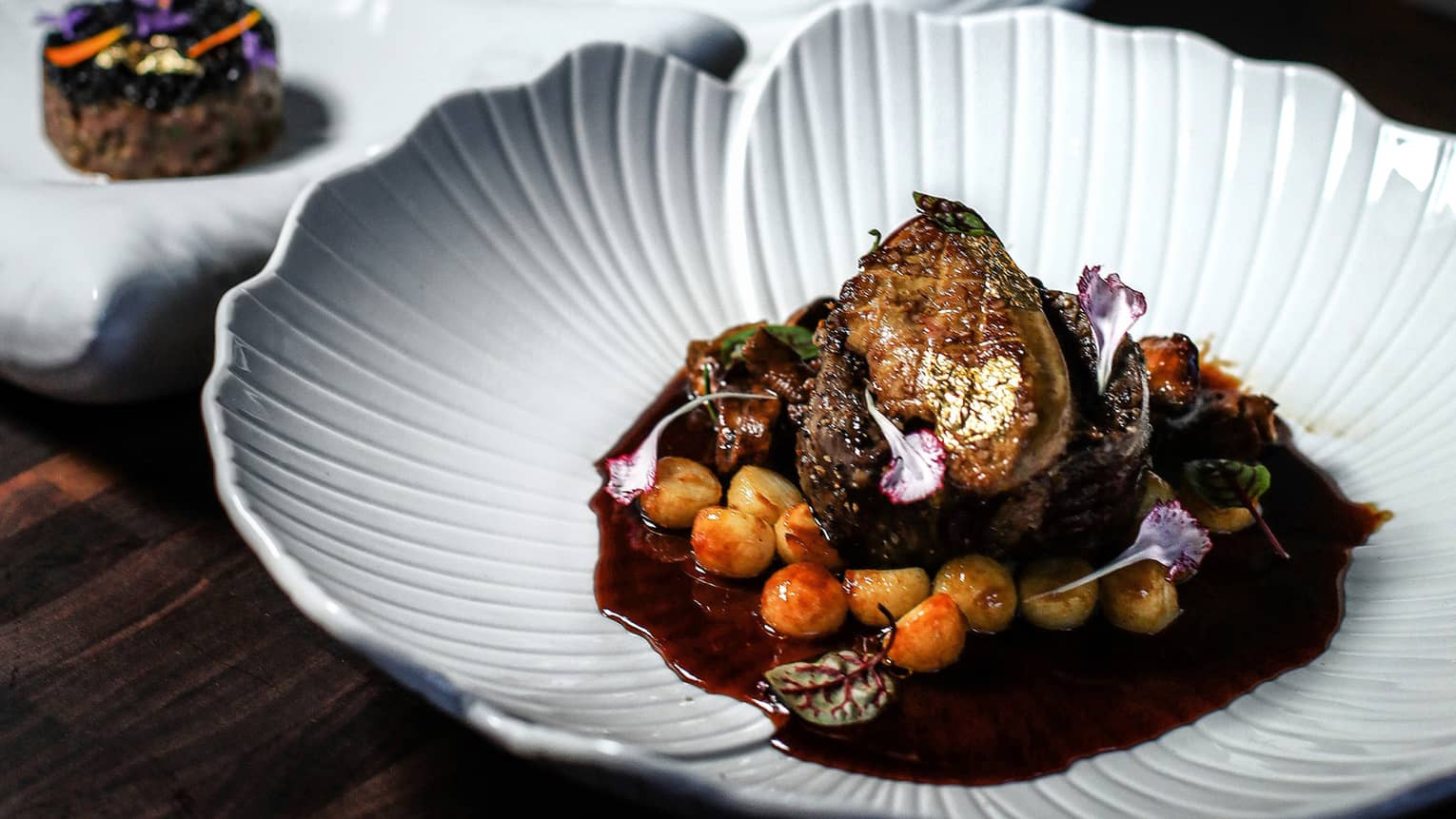 Three white plates of food set on a dark table with a dark backdrop