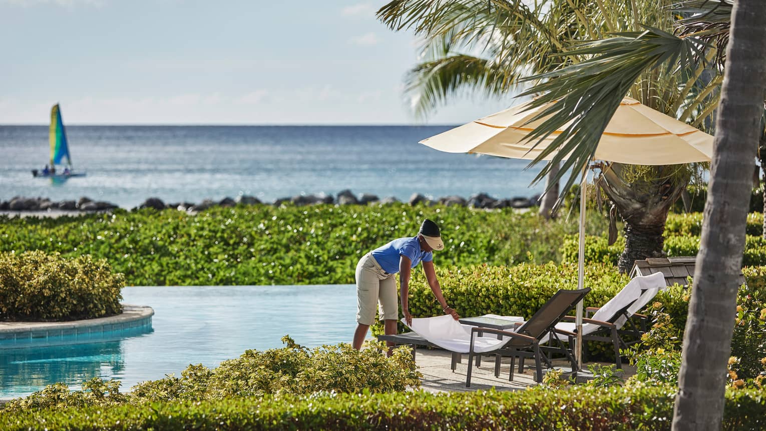 Hotel staff sets patio chair on Ocean Pool deck, boat sailing on Caribbean Sea