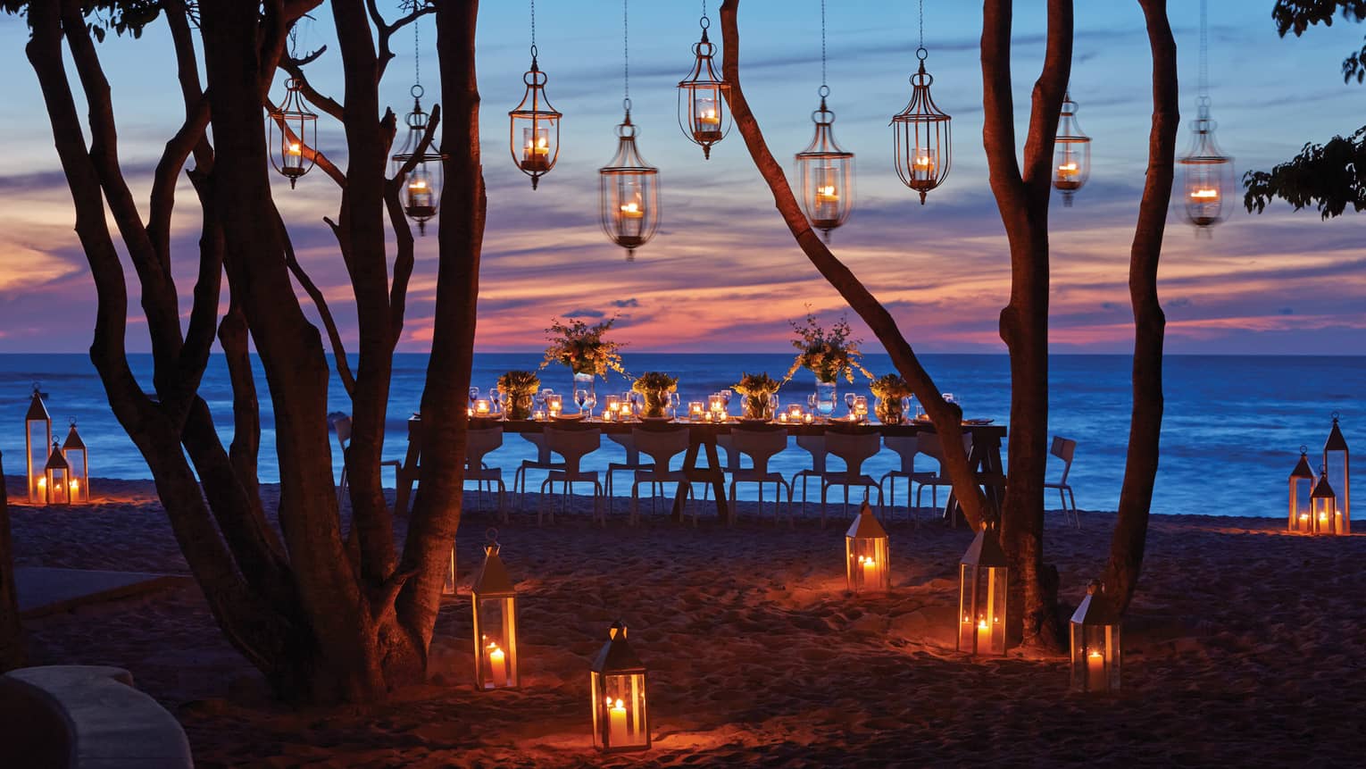 Lanterns hang from trees near dining table on Manzanillas Beach at sunset