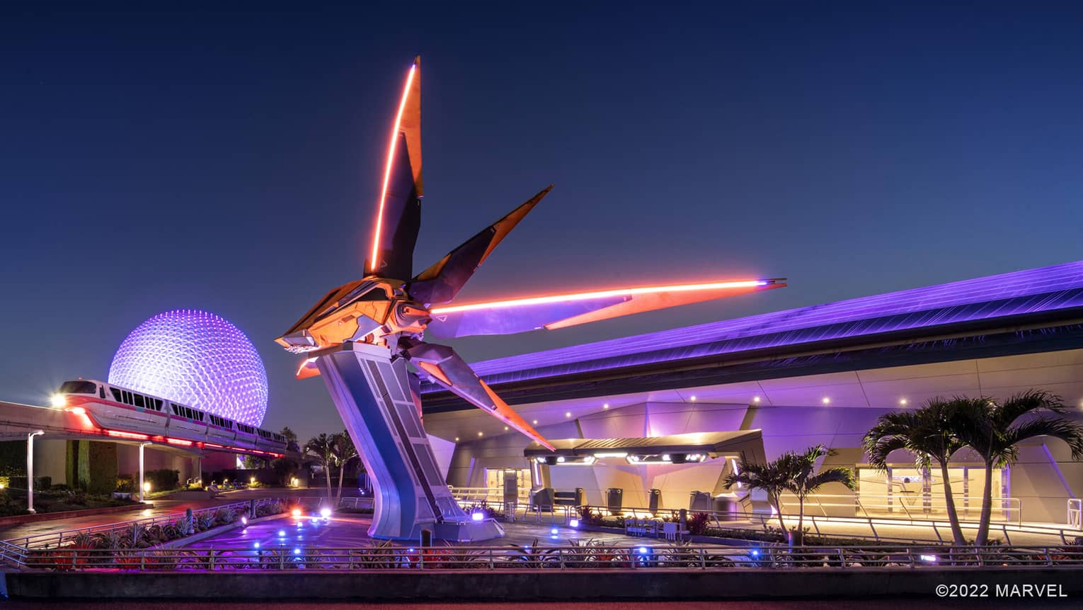 An orange and black sci-fi spaceship resting on a tall pedestal with a tram moving near it.