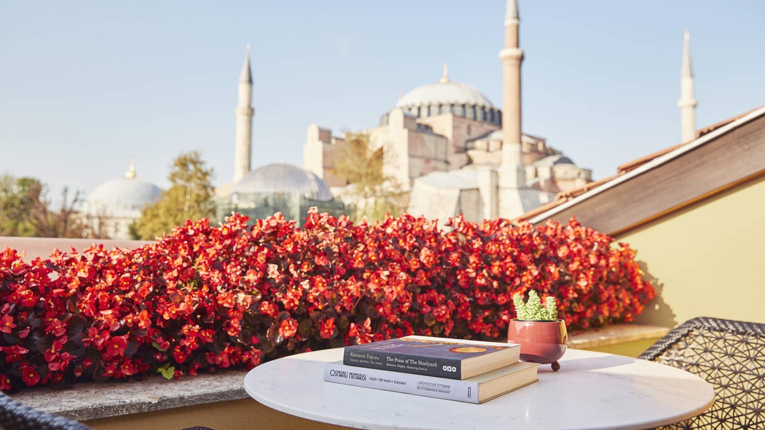 Hotel suite terrace with books on small round table beside red flowers and view of the Blue Mosque
