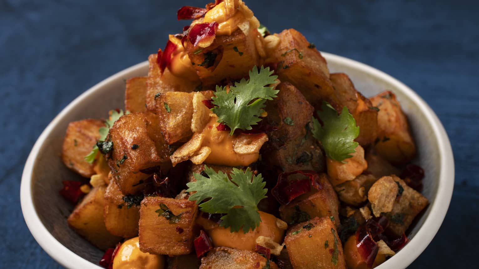 Batata Harra: Crispy layered potatoes with spicy hara coriander dip garnished with cilantro and seved in a white bowl