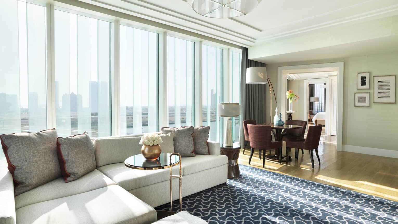 Deluxe Four Seasons Executive Suite large living room with L-shaped white sofa against large window, dining table
