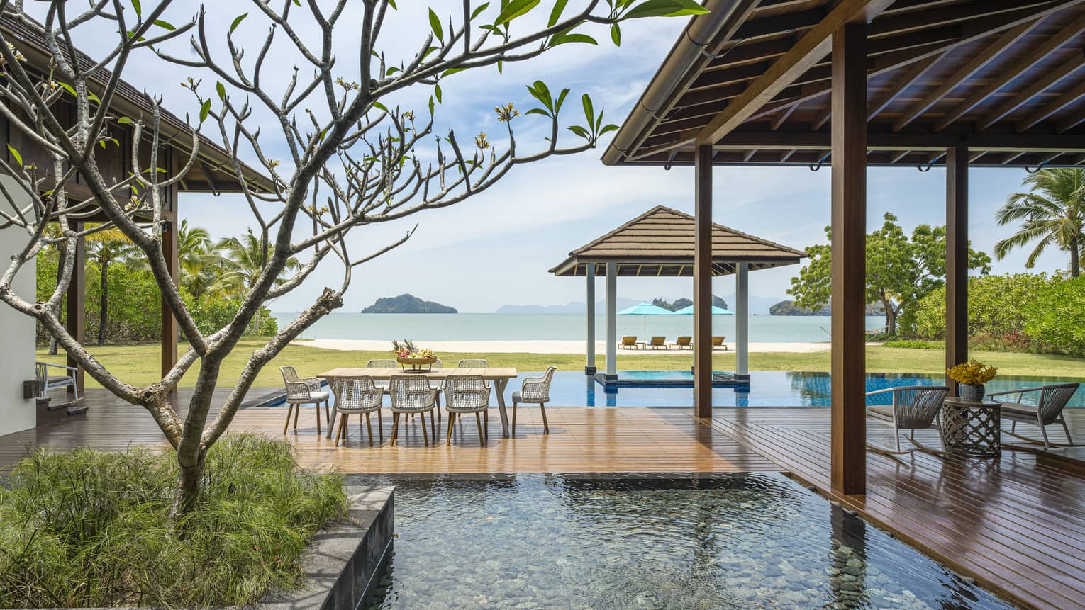 Wooden deck with dining table seemingly floating over a pool and pond