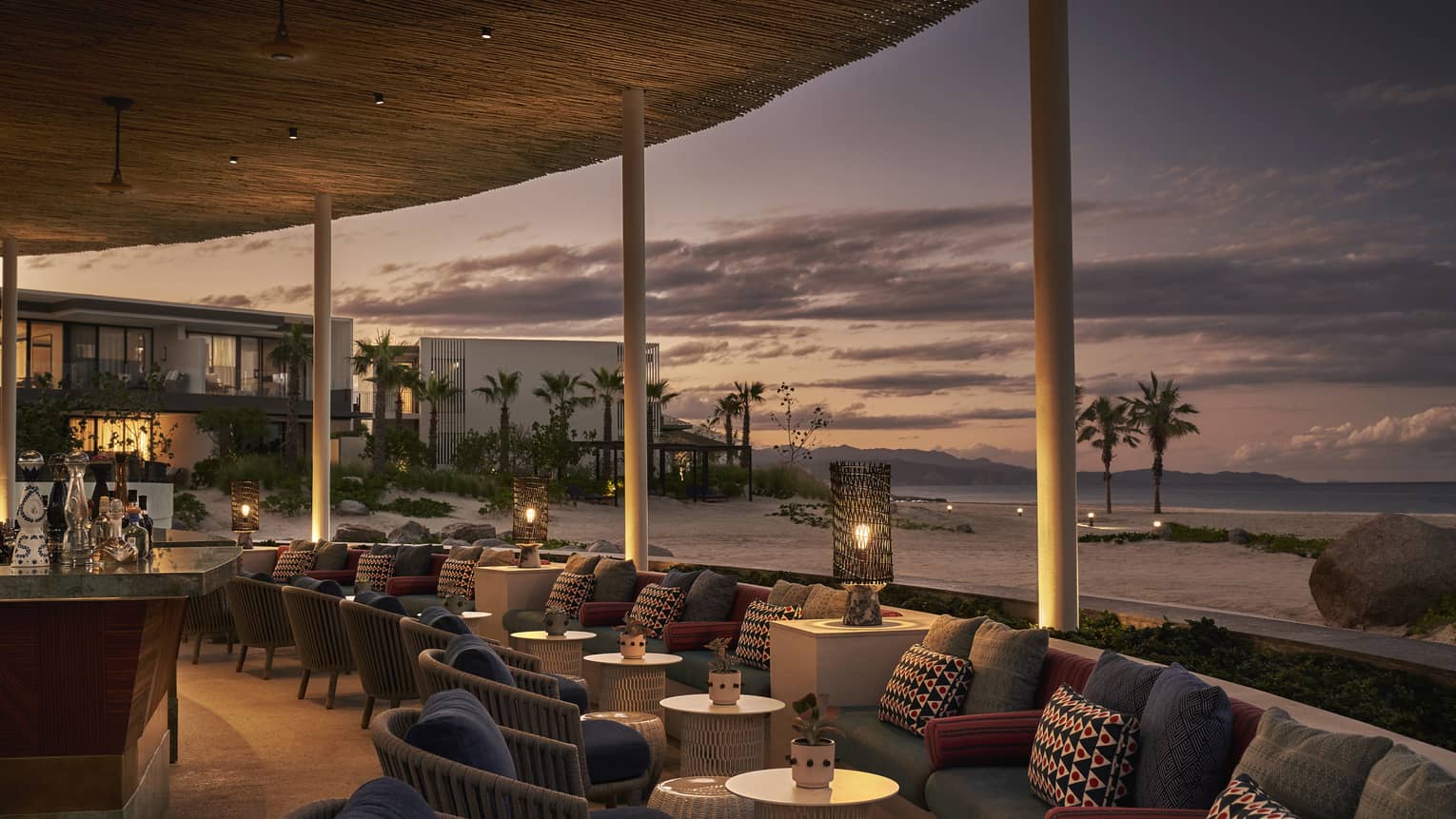 Dimly lit Casa de Brasa lounge area overlooking beach with palm trees at dusk