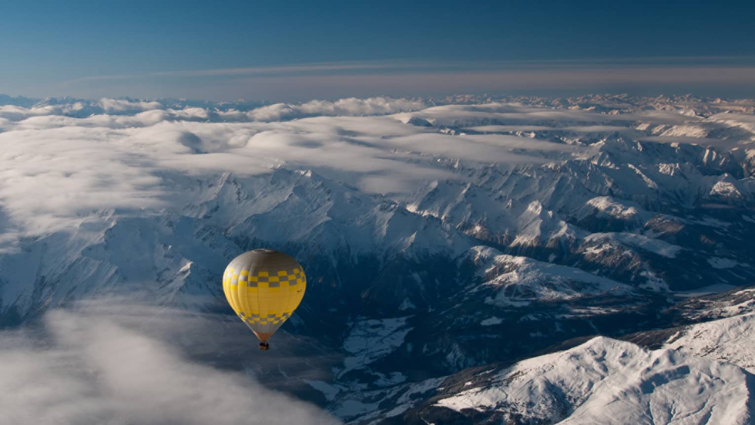 Yellow hot air balloon soaring over the snow-covered Alps