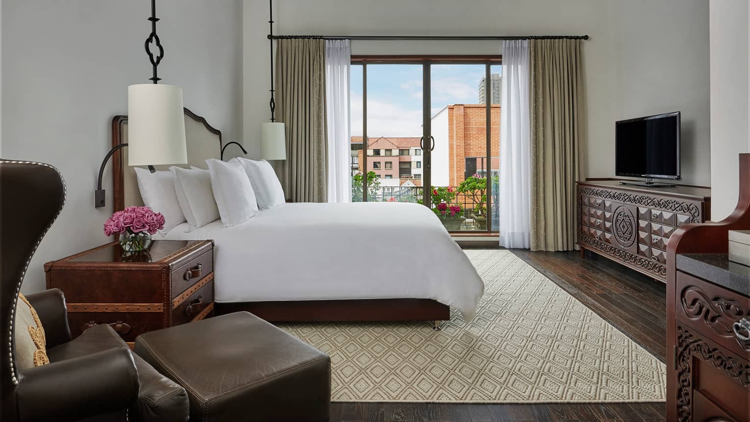 Superior room leather armchair, ottoman, trunk-style nightstand, hanging white lamps, bed by balcony door