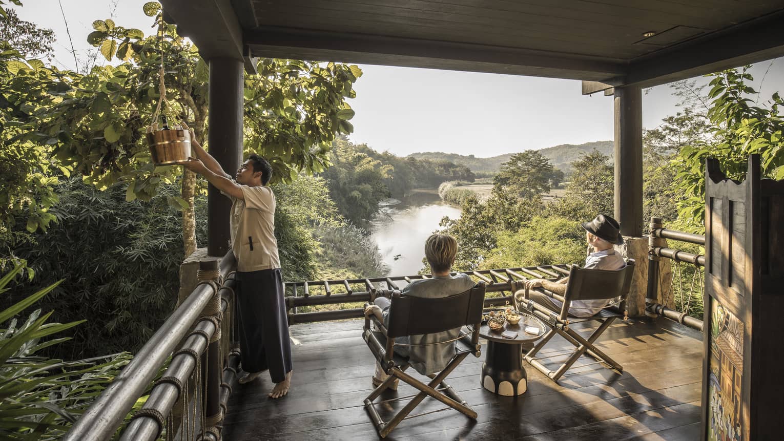 Couple, hotel staff on wood platform patio overlooking the lush Ruak River basin