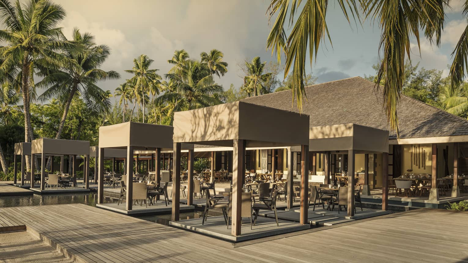 Outdoor Claudine restaurant with tables on decks over water, covered with wooden canopy 