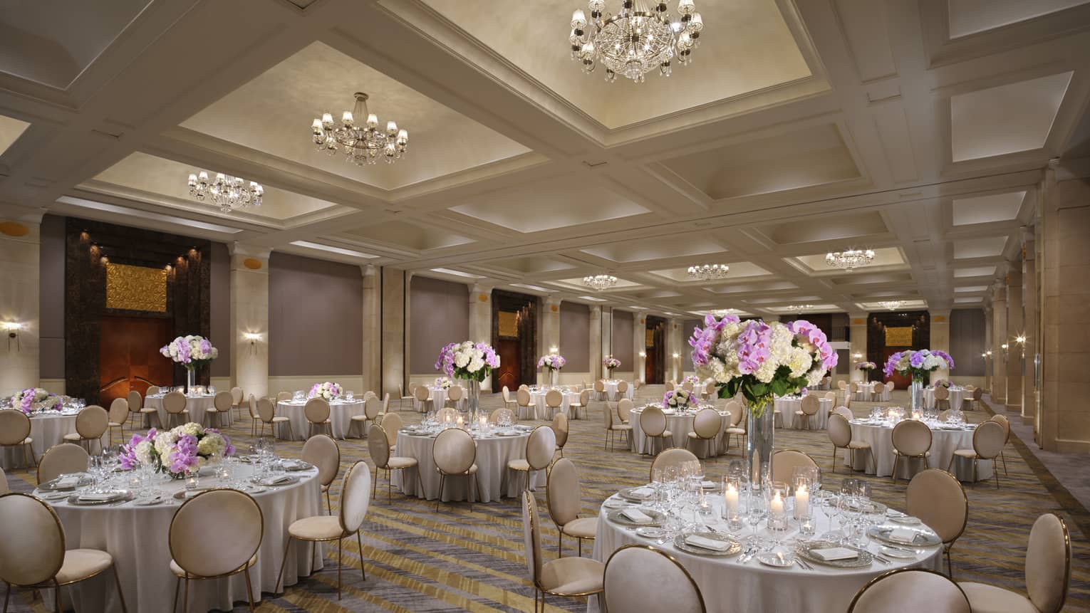 A chandelier-clad ballroom set with several circular tables boasting tall displays of hydrangeas. 