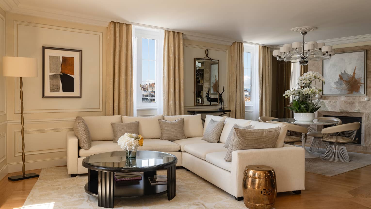 Luxury living room with a beige sectional sofa, coffee table, abstract wall art and dining area with a round table, cushioned chairs and floral arrangement