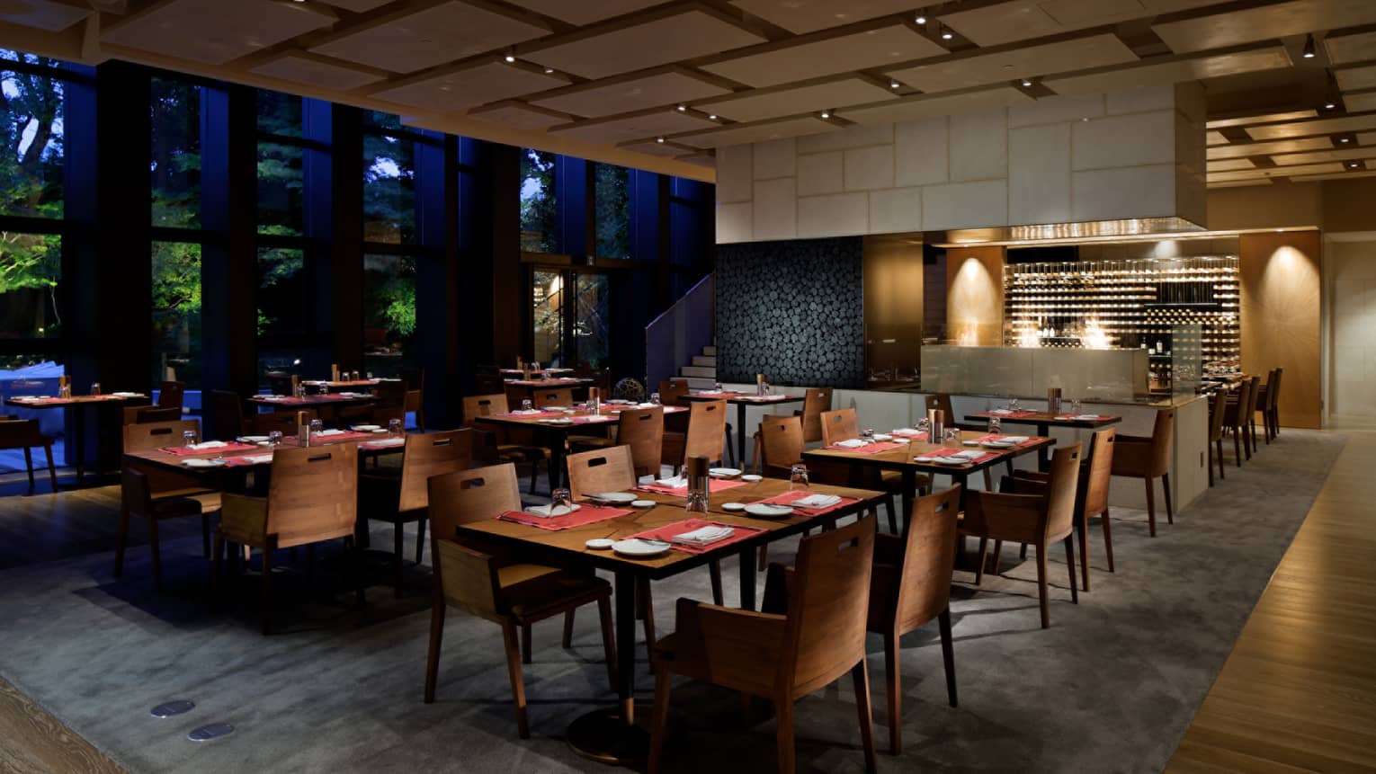 Brasserie dining tables, chairs in front of wine cellar, bar at night