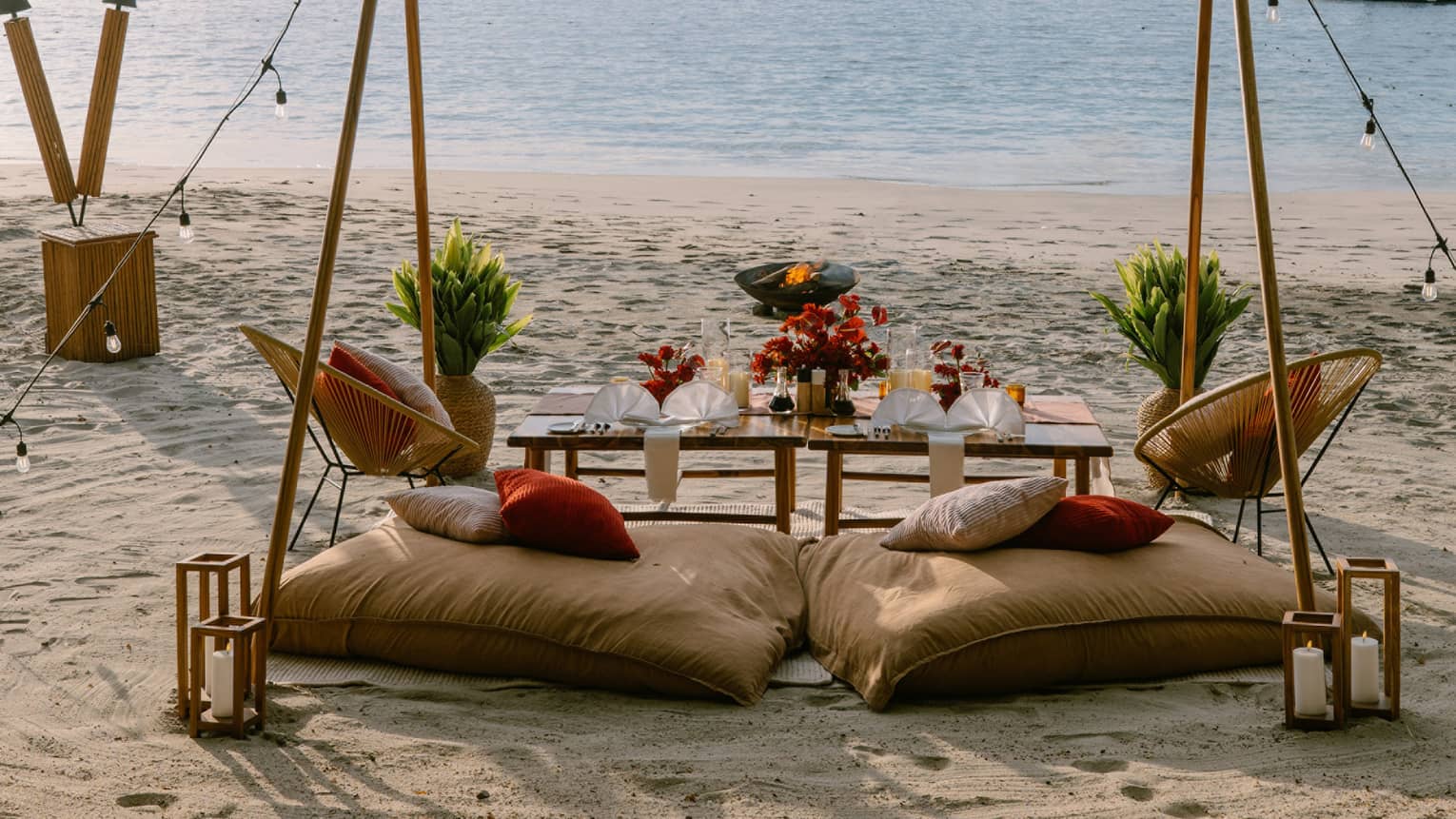 Private dining set up on a beach with two cusions, a table, string lights and rustic decorations
